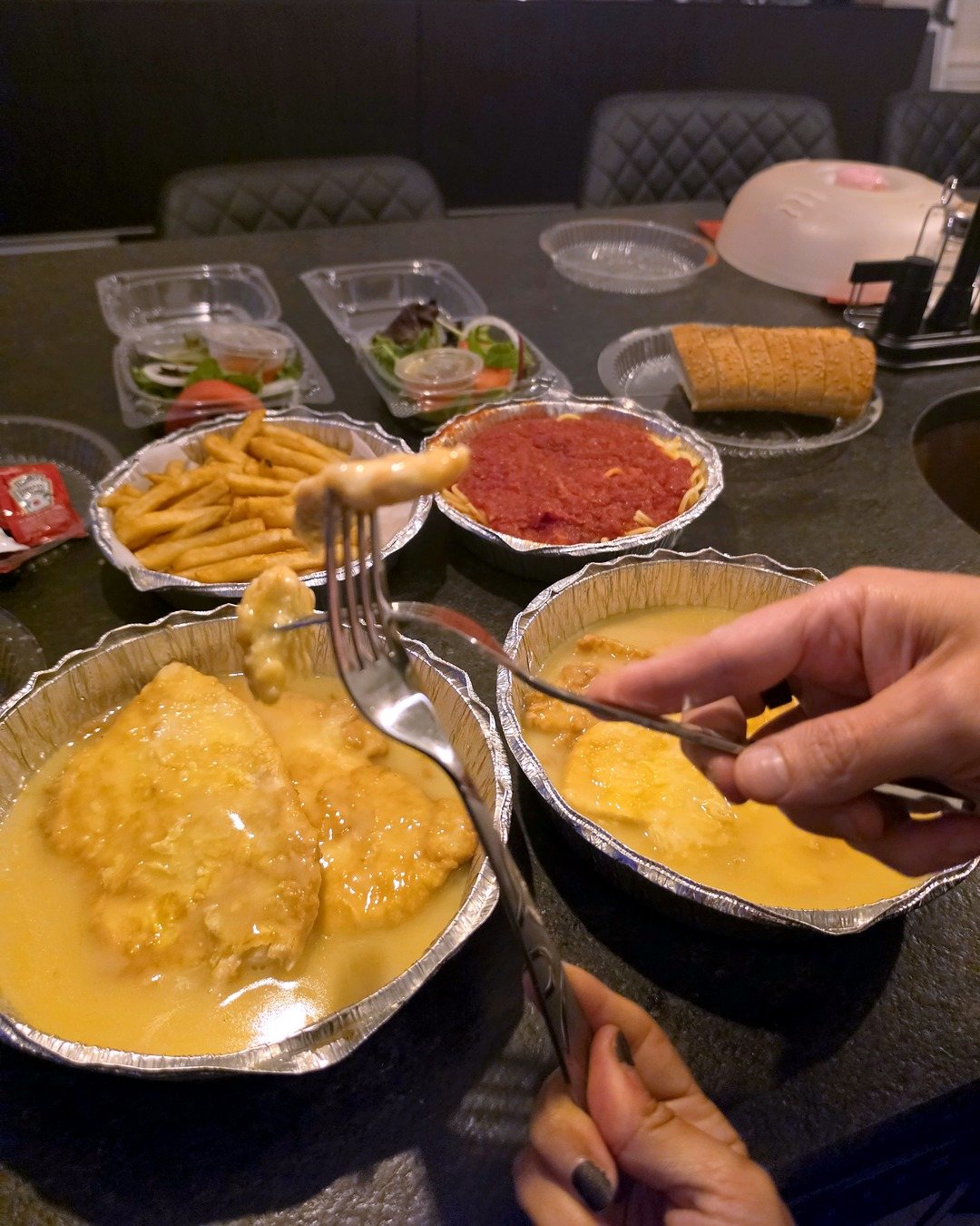 A forkful of chicken francese over the tray, with fries and spaghetti behind